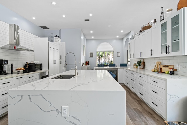 kitchen with light stone countertops, a center island with sink, and wall chimney range hood