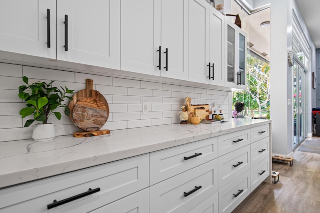 kitchen featuring white cabinets, backsplash, hardwood / wood-style flooring, and light stone countertops