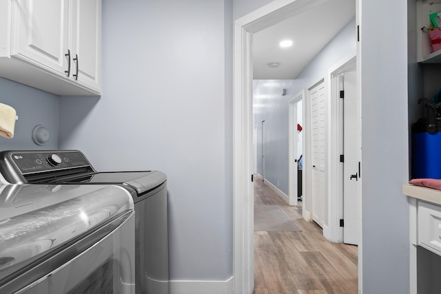 clothes washing area with cabinets, light wood-type flooring, and washer and clothes dryer