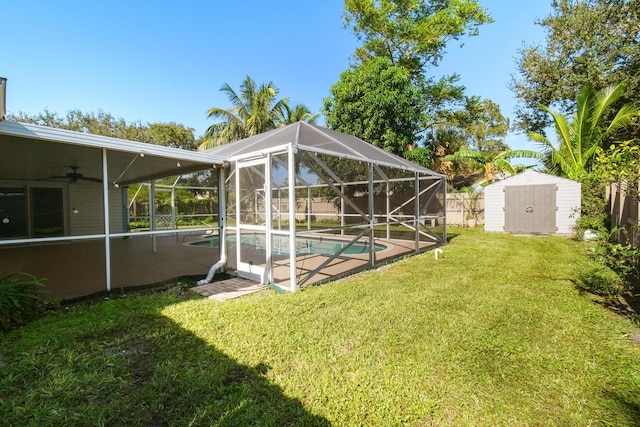 view of yard featuring ceiling fan, glass enclosure, a fenced in pool, and a shed