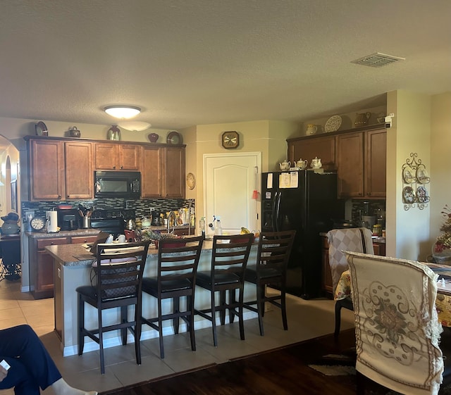 kitchen with tasteful backsplash, a breakfast bar, black appliances, stone countertops, and a kitchen island