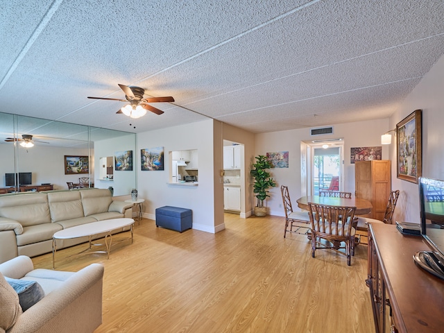 living room featuring ceiling fan, light hardwood / wood-style floors, and a textured ceiling