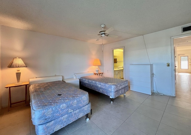 bedroom with ceiling fan, light tile patterned floors, a textured ceiling, and connected bathroom