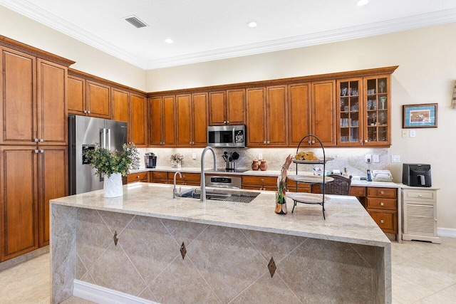 kitchen with stainless steel appliances, light stone counters, ornamental molding, and an island with sink