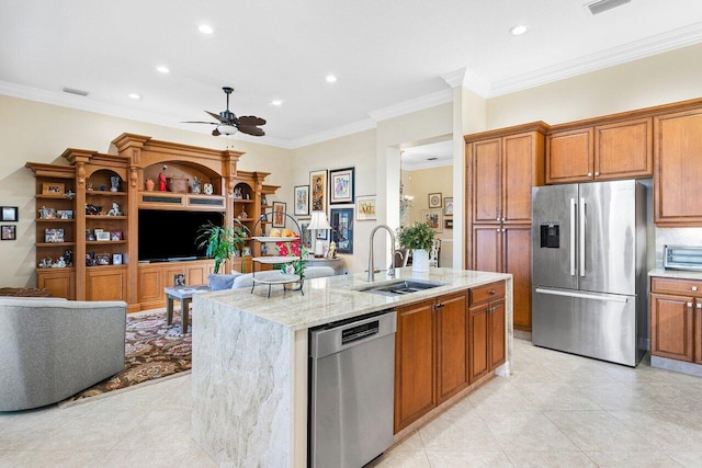 kitchen with appliances with stainless steel finishes, light stone counters, ornamental molding, a kitchen island with sink, and sink