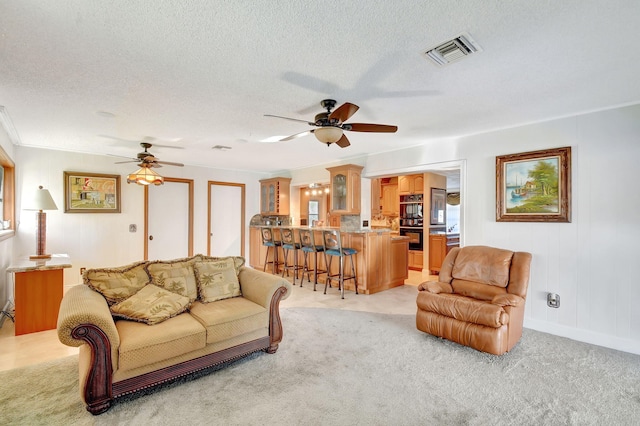 living room featuring a textured ceiling, light colored carpet, ceiling fan, and crown molding