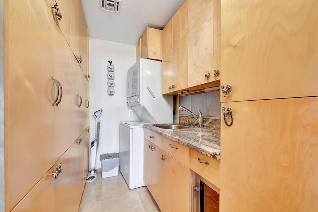 laundry room featuring cabinets, light tile patterned floors, stacked washer and dryer, and sink