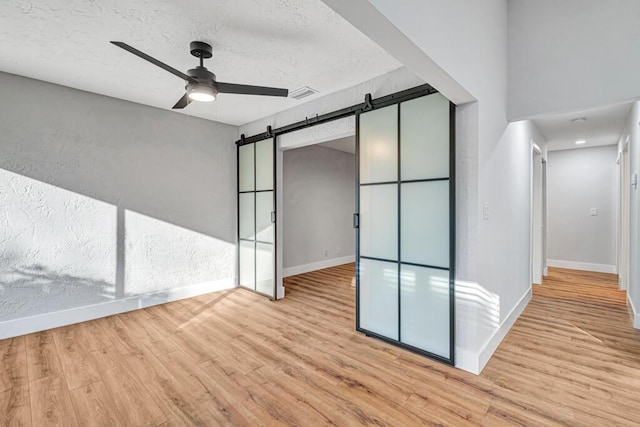 empty room featuring ceiling fan, a barn door, and light hardwood / wood-style flooring