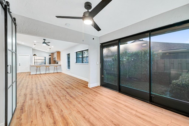 interior space featuring a barn door, ceiling fan, vaulted ceiling, and light wood-type flooring