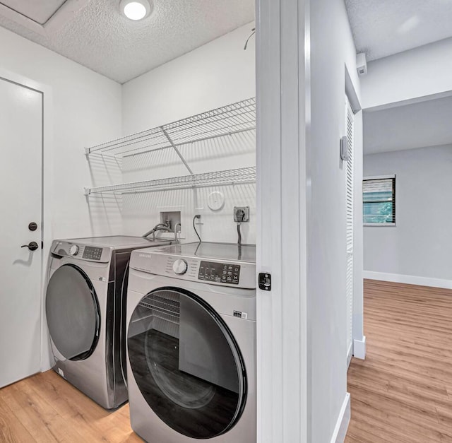 laundry room with light hardwood / wood-style floors, a textured ceiling, and washing machine and clothes dryer