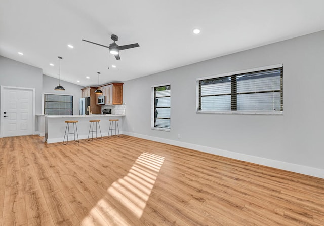 unfurnished living room featuring ceiling fan, light hardwood / wood-style flooring, vaulted ceiling, and sink