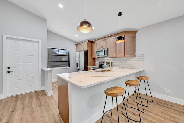 kitchen featuring kitchen peninsula, appliances with stainless steel finishes, a breakfast bar, decorative light fixtures, and light hardwood / wood-style floors