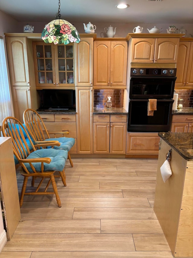 kitchen featuring pendant lighting, tasteful backsplash, black double oven, and light hardwood / wood-style flooring