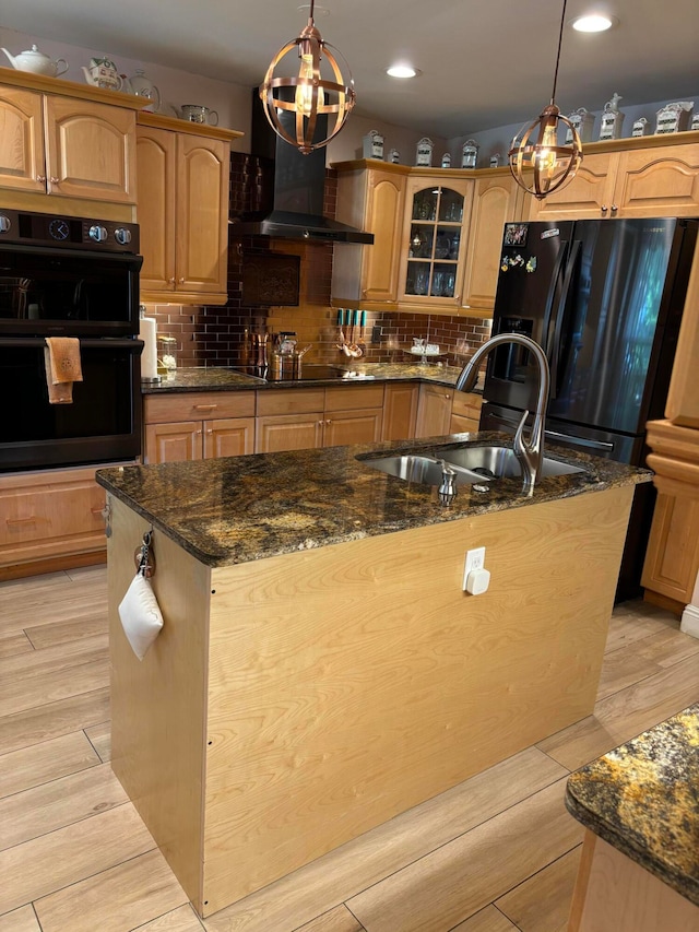 kitchen featuring dark stone countertops, decorative light fixtures, wall chimney exhaust hood, and light hardwood / wood-style floors