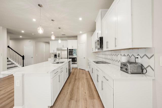 kitchen with pendant lighting, backsplash, a center island with sink, appliances with stainless steel finishes, and white cabinetry