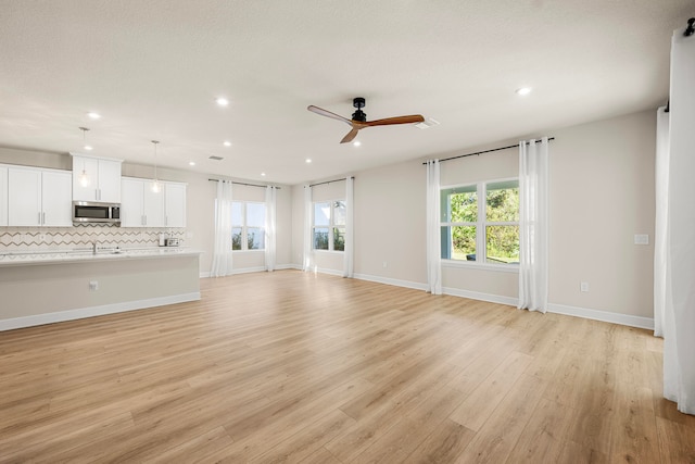 unfurnished living room featuring ceiling fan, light wood-type flooring, and sink