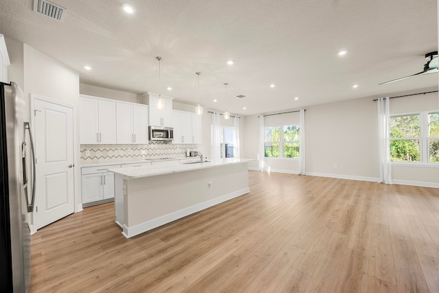 kitchen with pendant lighting, a kitchen island with sink, decorative backsplash, white cabinetry, and stainless steel appliances