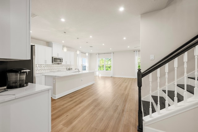 kitchen with light stone counters, sink, pendant lighting, white cabinetry, and an island with sink