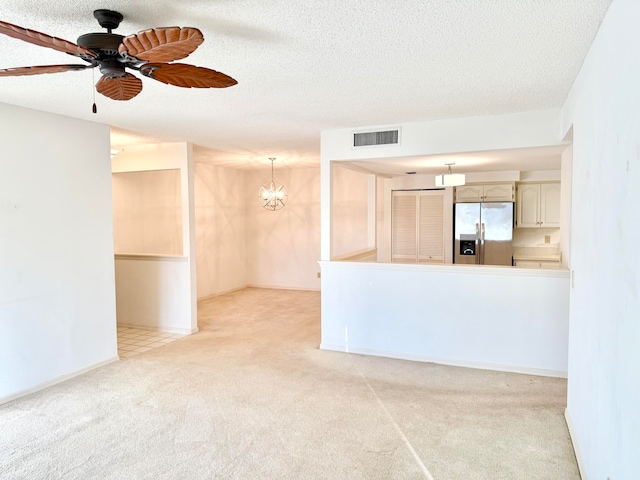 unfurnished living room featuring ceiling fan with notable chandelier, a textured ceiling, and light colored carpet