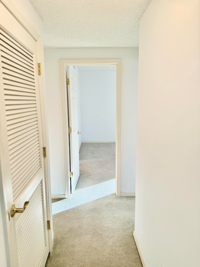 hallway featuring a textured ceiling and light colored carpet