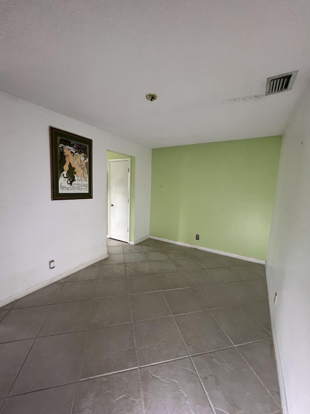 empty room featuring dark tile patterned floors, baseboards, and visible vents