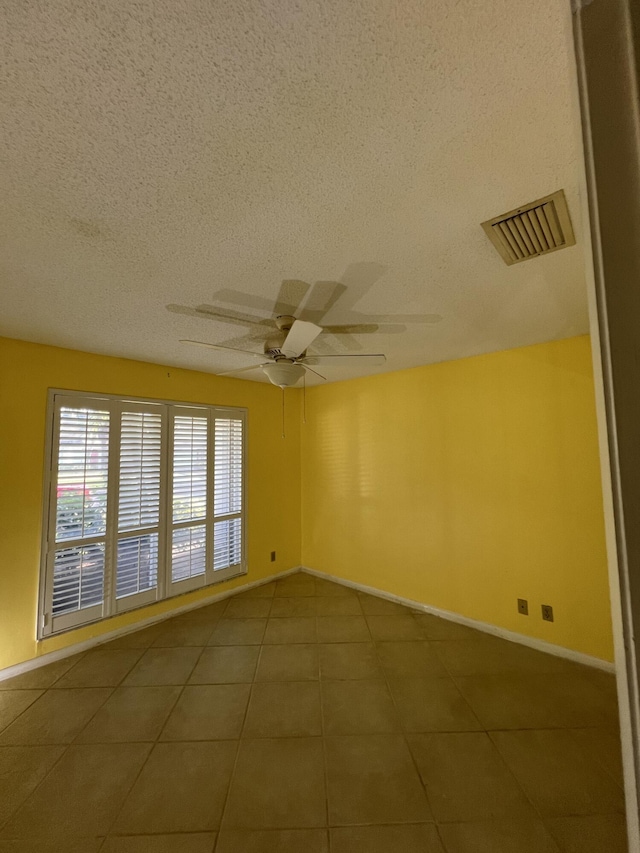 spare room featuring visible vents, a ceiling fan, a textured ceiling, baseboards, and tile patterned floors