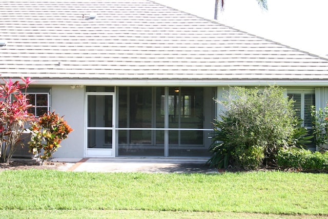 rear view of property featuring a yard, roof with shingles, and stucco siding