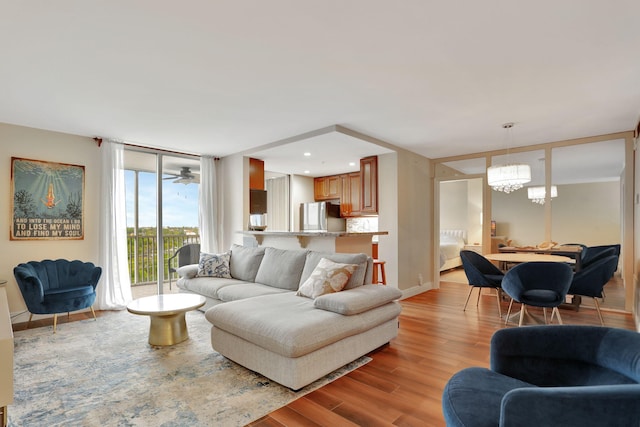 living room with floor to ceiling windows, ceiling fan with notable chandelier, and light wood-type flooring