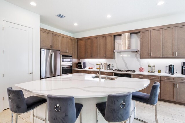 kitchen featuring wall chimney exhaust hood, a breakfast bar, stainless steel gas cooktop, sink, and a center island with sink