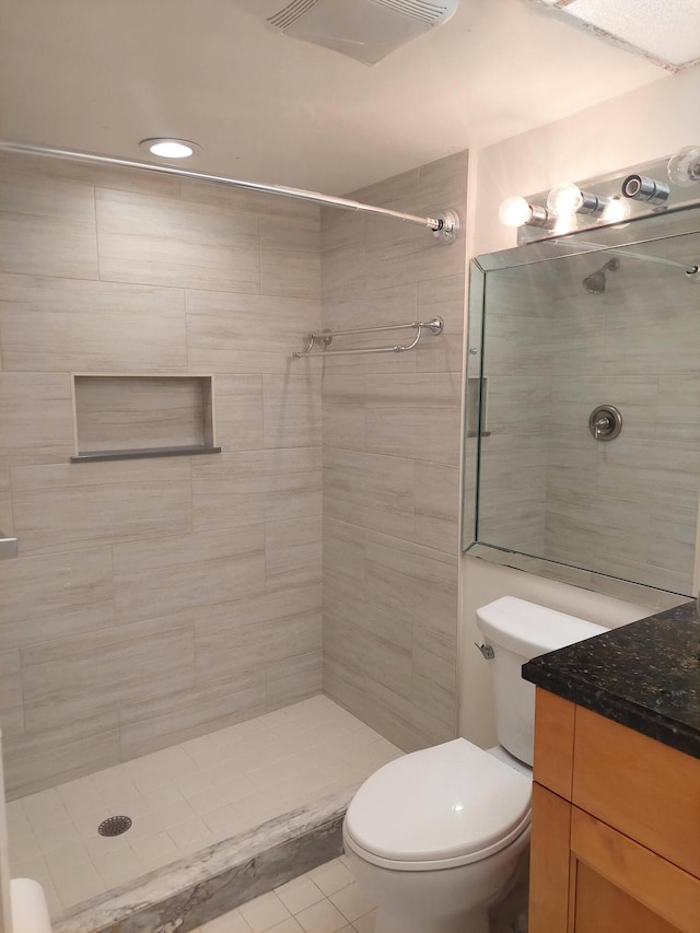 bathroom featuring a tile shower, tile patterned floors, vanity, and toilet