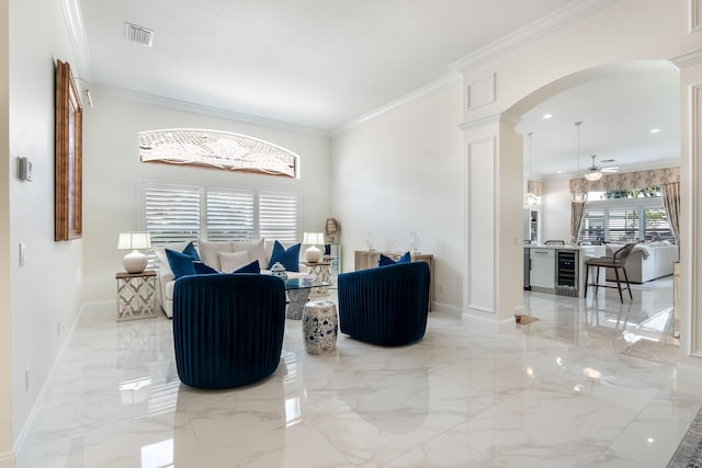 living area with beverage cooler, ornate columns, ceiling fan, and ornamental molding