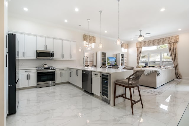 kitchen with kitchen peninsula, wine cooler, appliances with stainless steel finishes, decorative light fixtures, and white cabinetry