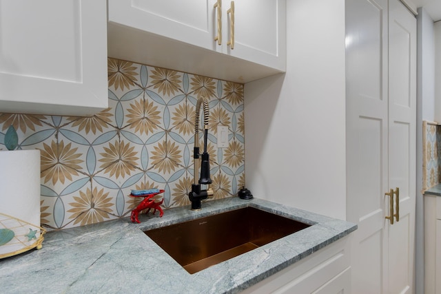 interior details featuring tasteful backsplash, light stone countertops, sink, and white cabinetry