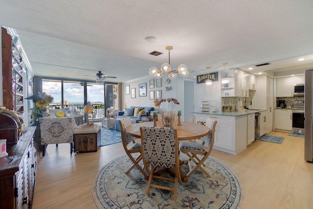 dining area featuring light wood-type flooring, sink, ceiling fan with notable chandelier, and a textured ceiling