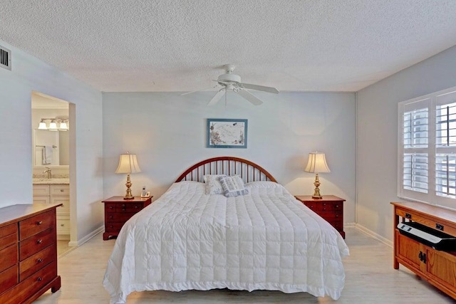 bedroom featuring a textured ceiling, connected bathroom, light hardwood / wood-style flooring, and ceiling fan