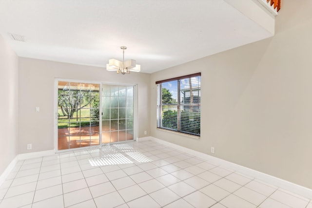 tiled spare room featuring plenty of natural light and an inviting chandelier