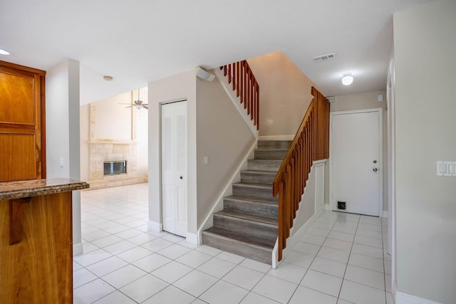 stairway with a fireplace, tile patterned floors, and ceiling fan