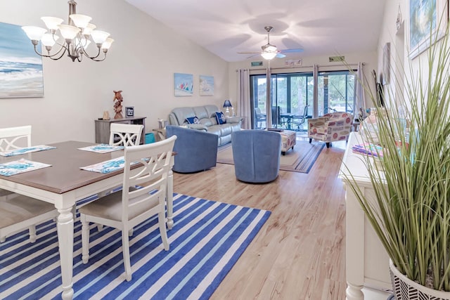 dining room with ceiling fan with notable chandelier, light hardwood / wood-style floors, and vaulted ceiling