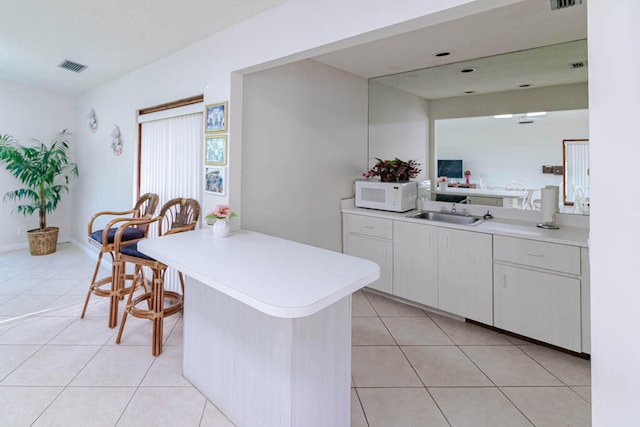 kitchen featuring sink, kitchen peninsula, light tile patterned flooring, white cabinetry, and a breakfast bar area