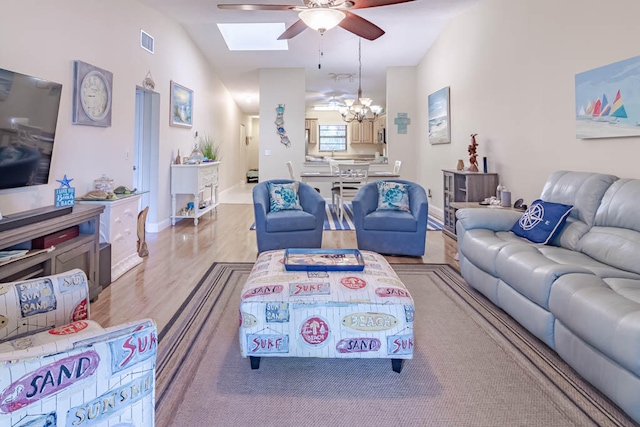 living room featuring lofted ceiling with skylight, light hardwood / wood-style flooring, and ceiling fan with notable chandelier