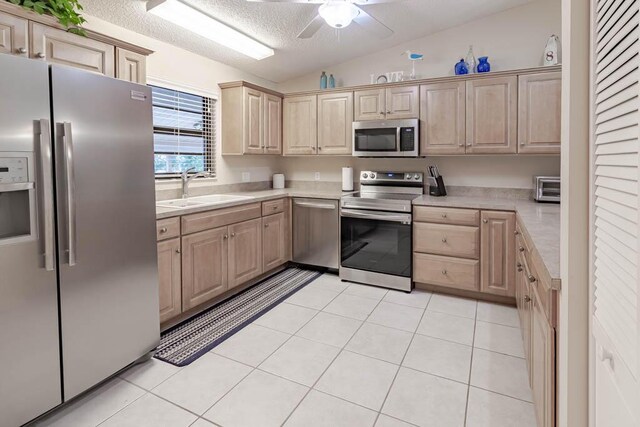 kitchen with light brown cabinets, sink, stainless steel appliances, lofted ceiling, and light tile patterned floors