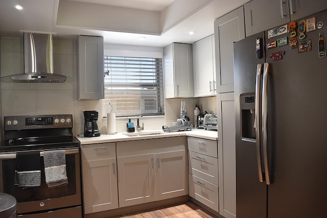 kitchen featuring appliances with stainless steel finishes, a raised ceiling, sink, wall chimney range hood, and light hardwood / wood-style floors