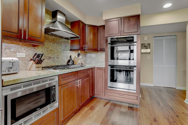 kitchen featuring wall chimney exhaust hood, decorative backsplash, stainless steel appliances, and light hardwood / wood-style flooring