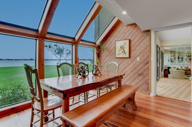 dining space with wooden walls, a water view, lofted ceiling with skylight, and light wood-type flooring