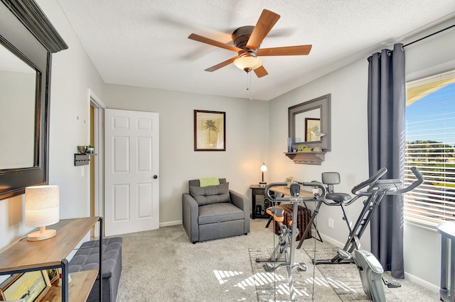 exercise room featuring ceiling fan, light carpet, and a textured ceiling