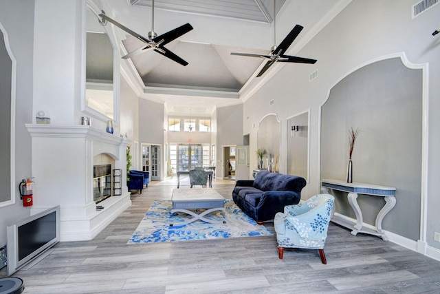 living room featuring a high ceiling, a premium fireplace, ceiling fan, and light hardwood / wood-style flooring