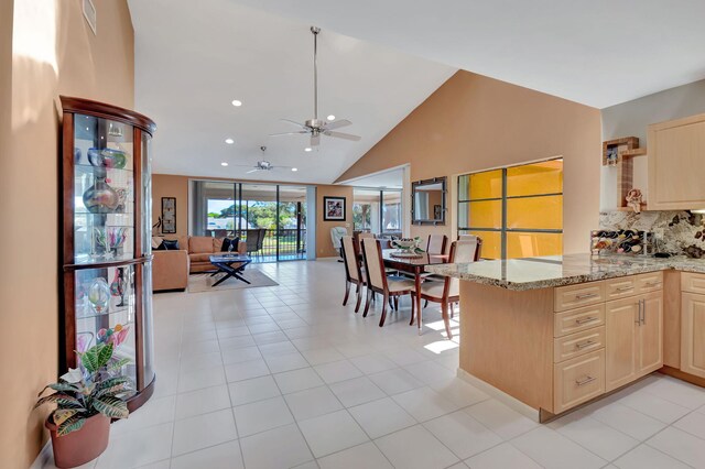 kitchen with kitchen peninsula, light stone counters, light brown cabinets, high vaulted ceiling, and light tile patterned flooring