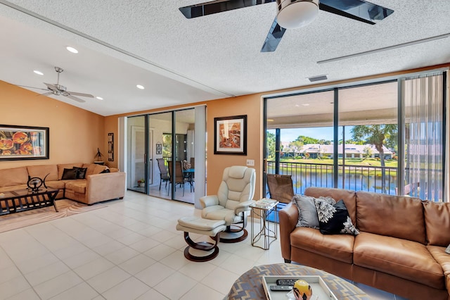 tiled living room with expansive windows, a textured ceiling, vaulted ceiling, ceiling fan, and a water view