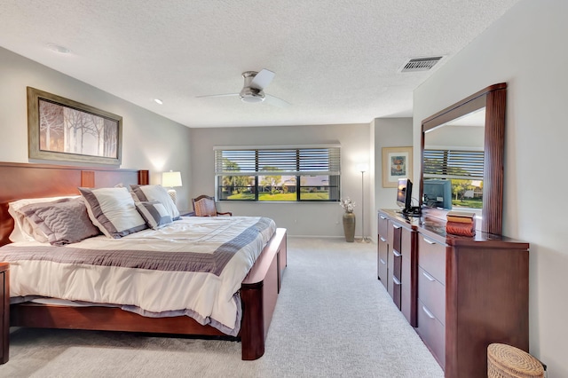 bedroom with ceiling fan, light colored carpet, and a textured ceiling