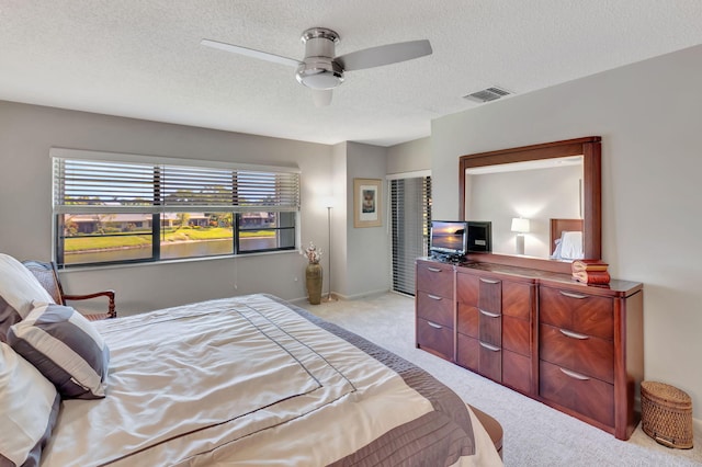 bedroom with a textured ceiling, light colored carpet, and ceiling fan